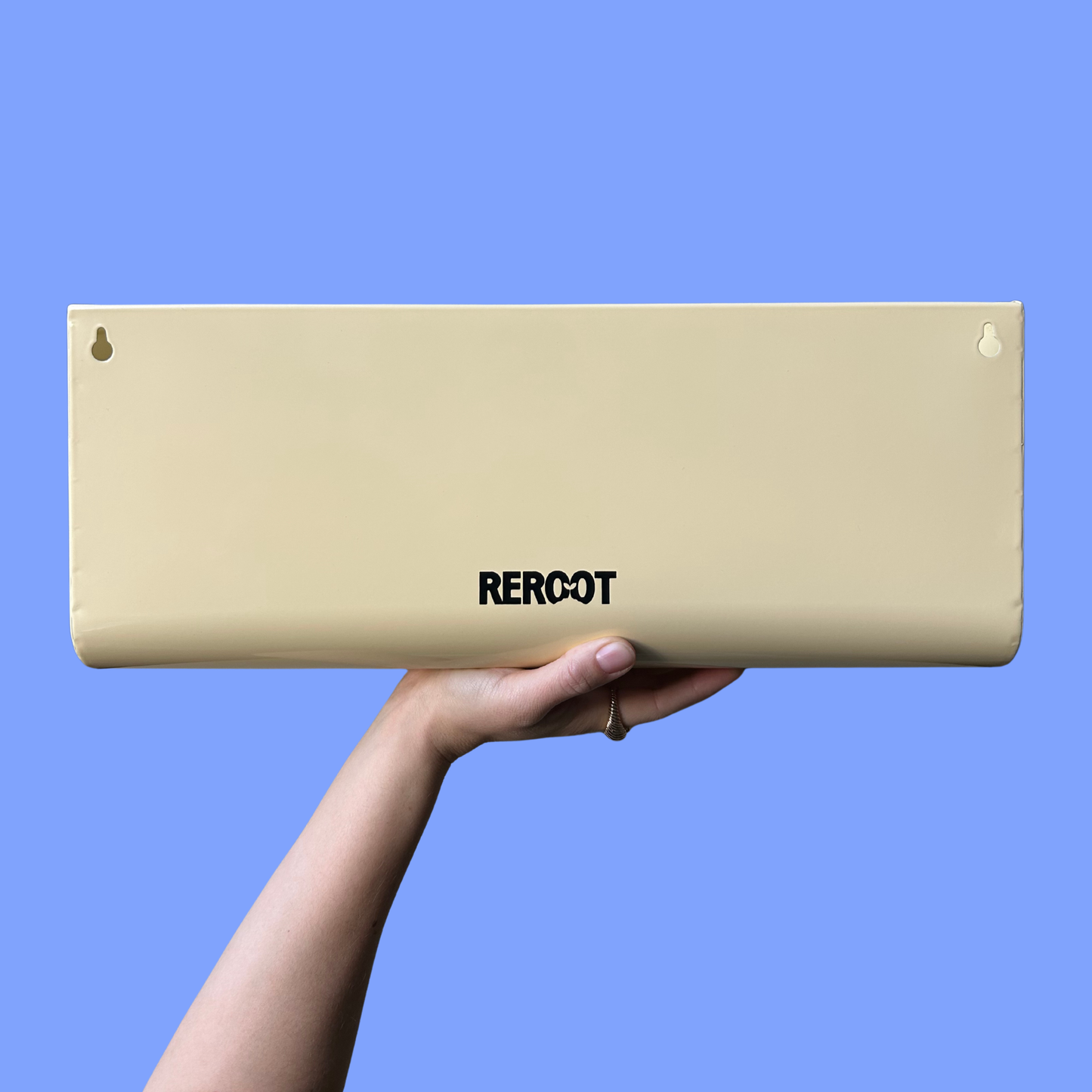 Empty cream stainless steel planter held by a person's hand against a blue background.